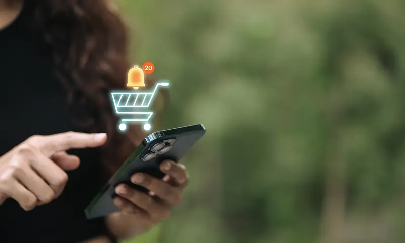 Finger tippt auf ein Smartphone, darüber ein Einkaufswagen-Symbol mit Benachrichtigung