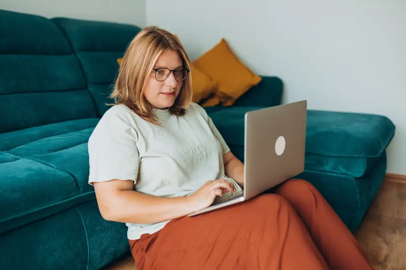 Frau mit Brille arbeitet am Laptop auf einem grünen Sofa